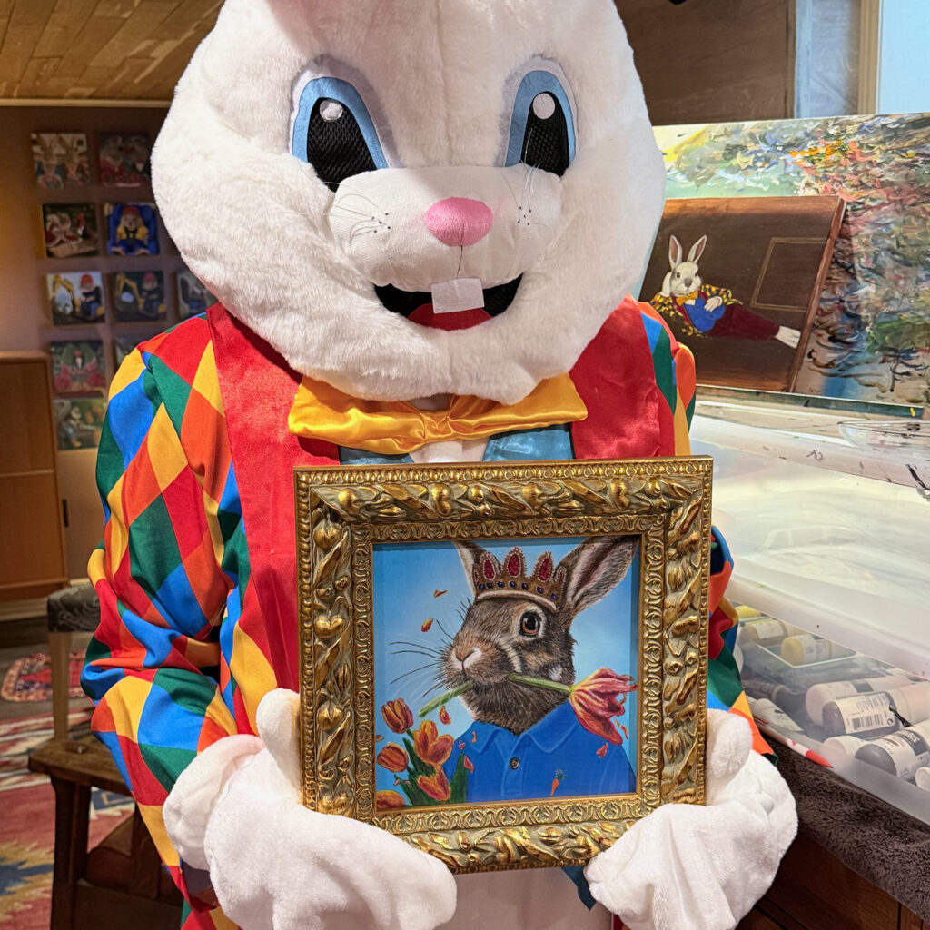 The Bloomin Fool holding an 8x8 inch acrylic painting of a rabbit in formal wear eating tulips.